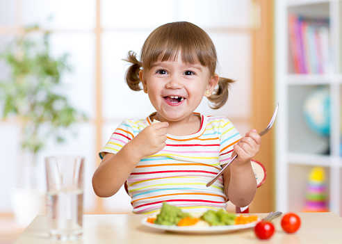 smiling kid girl eating healthy vegetables at kitchen