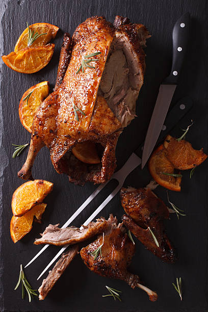 Cutting the roast duck and oranges on slate board. vertical