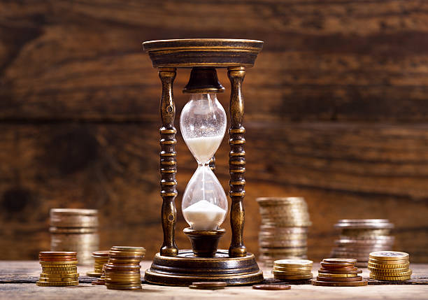 istock hourglass and coins on wooden background 601392044
