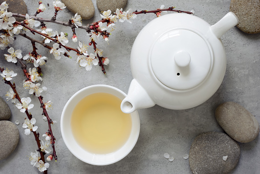 Tea concept, cup with tea and white teapot decorated with blooming spring tree branch, top view