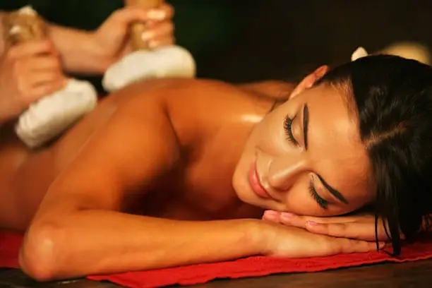 Young woman lying on wooden spa bed. Poultice hot herbal massage in spa salon.