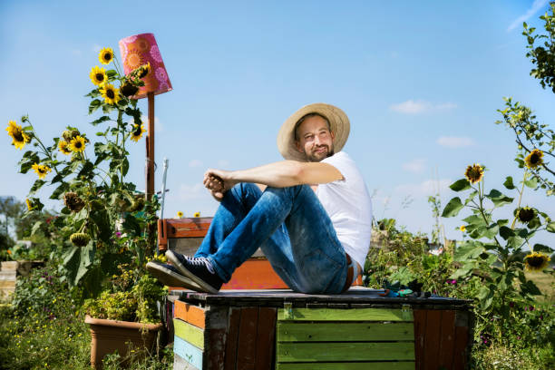 Smiling man resting on abandoned wooden table in yard against sky