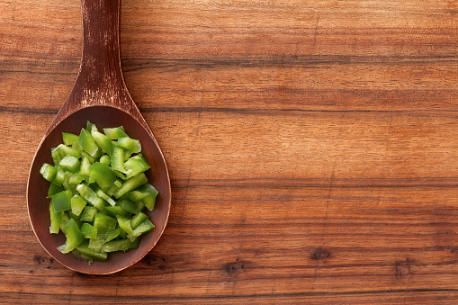 Top view of wooden spoon over table with diced green bell pepper on it