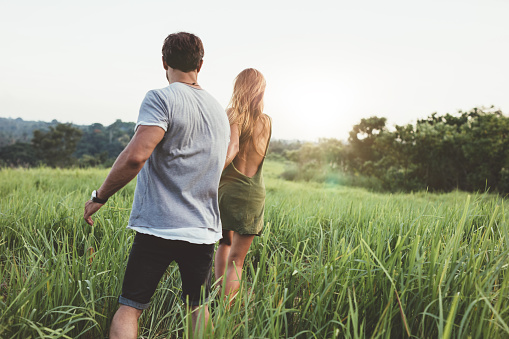 Rear view of a young couple strolling in a grass field. Young man and woman walking together in rural landscape.