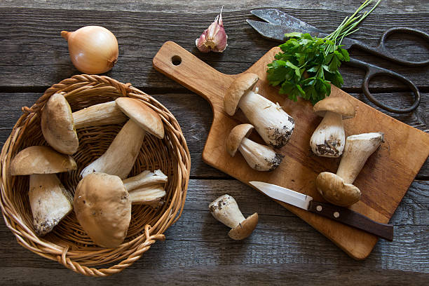 Fresh white mushrooms in basket on a rustic wooden board. Fresh white mushrooms in basket and ingredients for mushroom's cream-soup on a rustic wooden board, overhead view. porcini mushroom stock pictures, royalty-free photos & images
