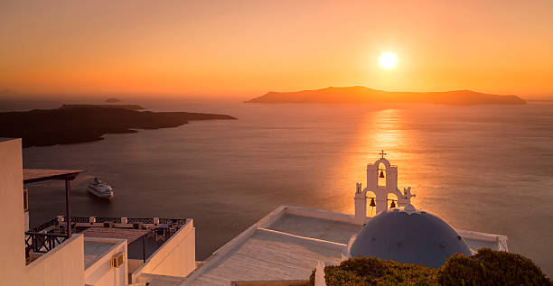 Summer sunset in Santorini island in Greece From high ground view point, a majestic sunset takes place in the horizon of the Santorini volcanic caldera. The blue dome accompanied with a bell tower, which is the symbol of the Cyclades islands in Greece, sits right on the brightly sun lit surface of the sea. fira santorini stock pictures, royalty-free photos & images