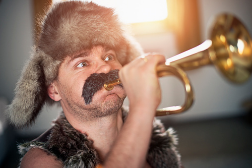 Portrait of a stereotypical eastern european polish or russian man playing trumpet with effort. The man is aged 35-40 years and is wearing big moustache and fur hat. 
