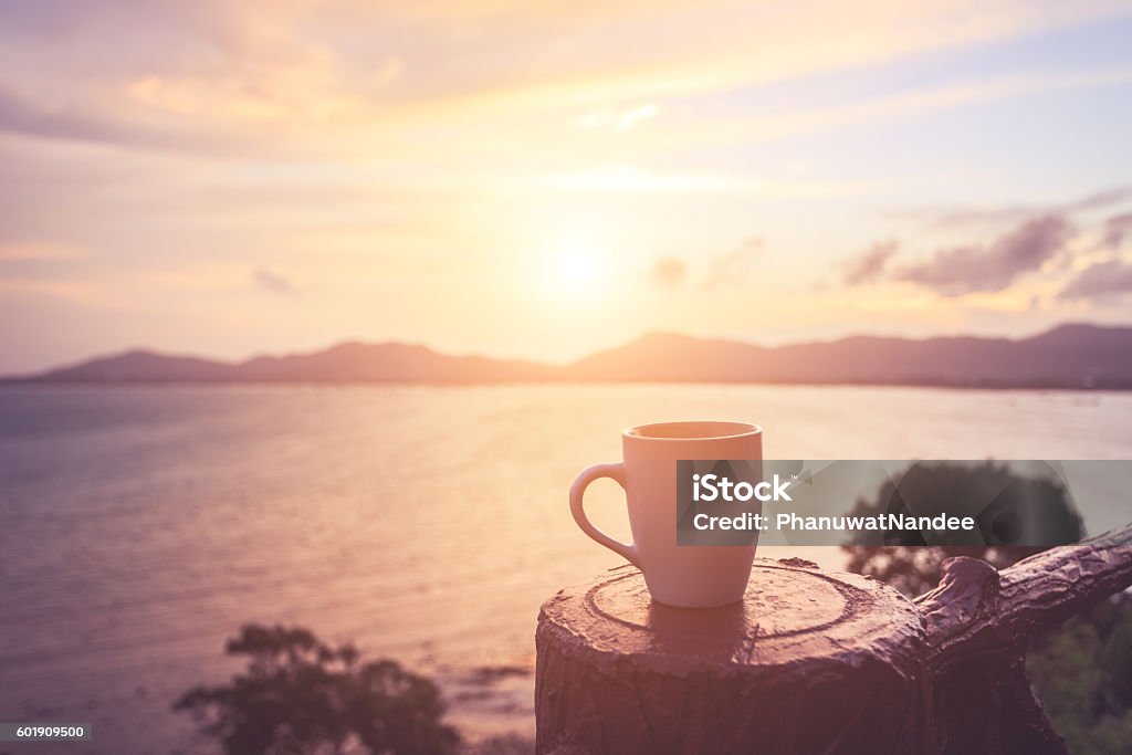 Coffee cup at sunset or sunrise beach Close up coffee cup at sunset or sunrise beach in the with lens flare. Warm toning effect. Retro and vintage style Coffee - Drink Stock Photo