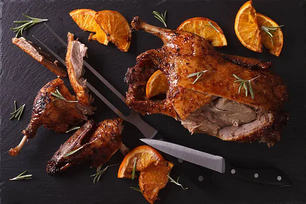 Photo of Cutting the roast duck and oranges on slate board. Horizontal