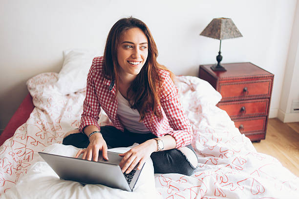 istock Smiling young woman sitting on bed and using laptop 601910216