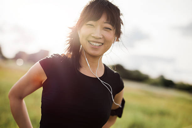 donna felice che corre in piedi all'aperto e sorride - running jogging asian ethnicity women foto e immagini stock