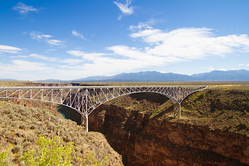 Taos, NM: Rio Grande Gorge Bridge under blue cloudy sky. The bridge, finished in 1965,  is on US 64 and the seventh highest bridge in the US.