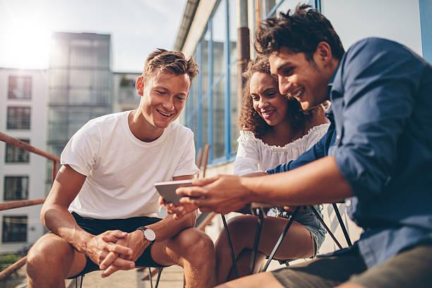 携帯電話でビデオを見ている人々のグループ - smart casual outdoors friendship happiness ストックフォトと画像