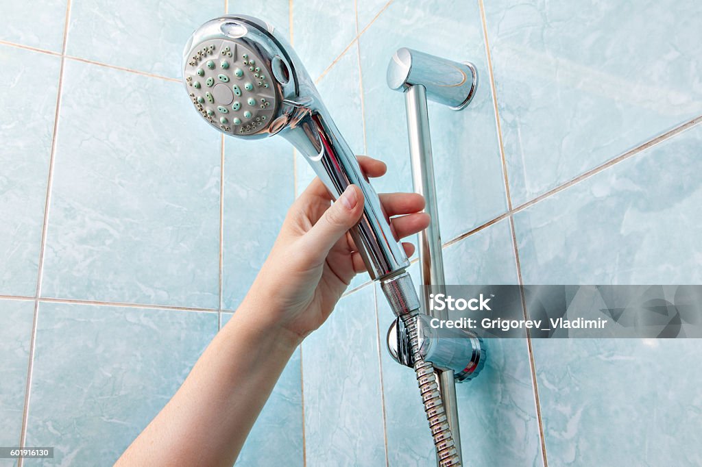 Close-up of human hand adjusts holder shower head with hose. Replacing the plumbing in the bathroom, close-up wall mounted hand shower and hose holder with height adjustable bar slider rail, human hand holding a shower head. Shower Head Stock Photo