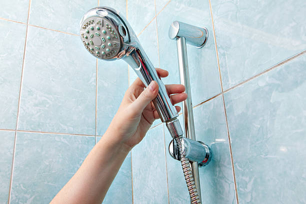 крупным планом человеческой руки регулирует держатель душем головку с шлангом. - hand shower стоковые фото и изображения