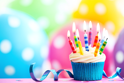 Vanilla buttercream cupcake with pink icing, sprinkles and gold 40th birthday candles. \nShot  on a light blue background with defocused lights.