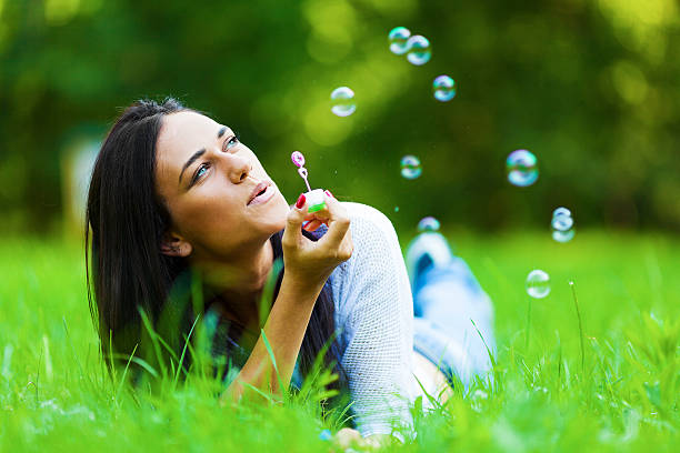 Young beautiful woman in park Young beautiful woman in park lying on front blowing bubbles. About 20 years old, Caucasian brunette. women lying down grass wood stock pictures, royalty-free photos & images