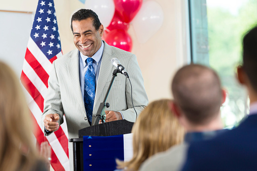 Senior adult African American man is smiling and answering questions while giving speech from podium. Candidate is running for local government office or city council.