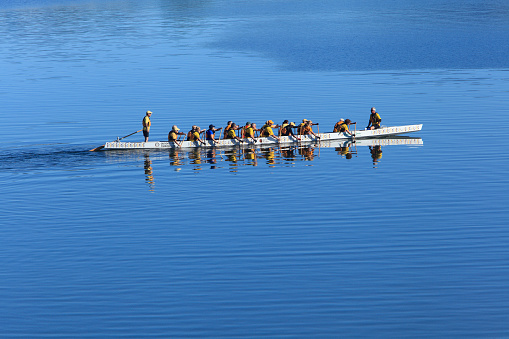 Osoyoos,Canada-June 17,2016: Group of men and women practicing rowing as a team. Blue background of water surrounding them totally. Helmsmen standing and sitting at either end. 