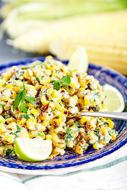 Homemade Mexican Corn Salad Close up of homemade vegetarian mexican street food corn salad with cilantro, lime, mayonnaise, garlic, chili and cheese on blue plate on stone background. Two corn heads on blured background corn salad stock pictures, royalty-free photos & images