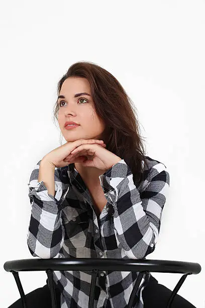 Awesome caucasian attractive sexy professional female model with brown hair posing in studio wearing casual shirt and black ragged jeans, sitting on chair, smiling, isolated on white background