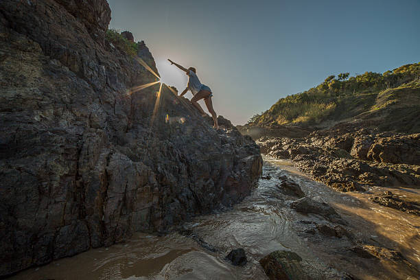 Young woman climbs steep rock, towards sunlight