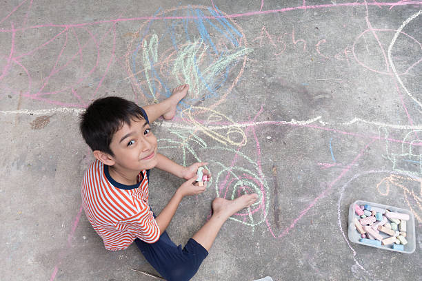 istock Little boy drawing and coloring by chalk on the ground 601937558