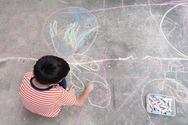 istock Little boy drawing and coloring by chalk on the ground 601937726