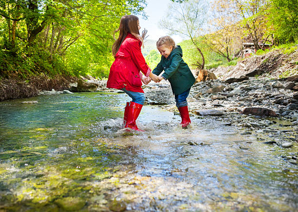 Happy children wearing rain boots jumping into a mountain river