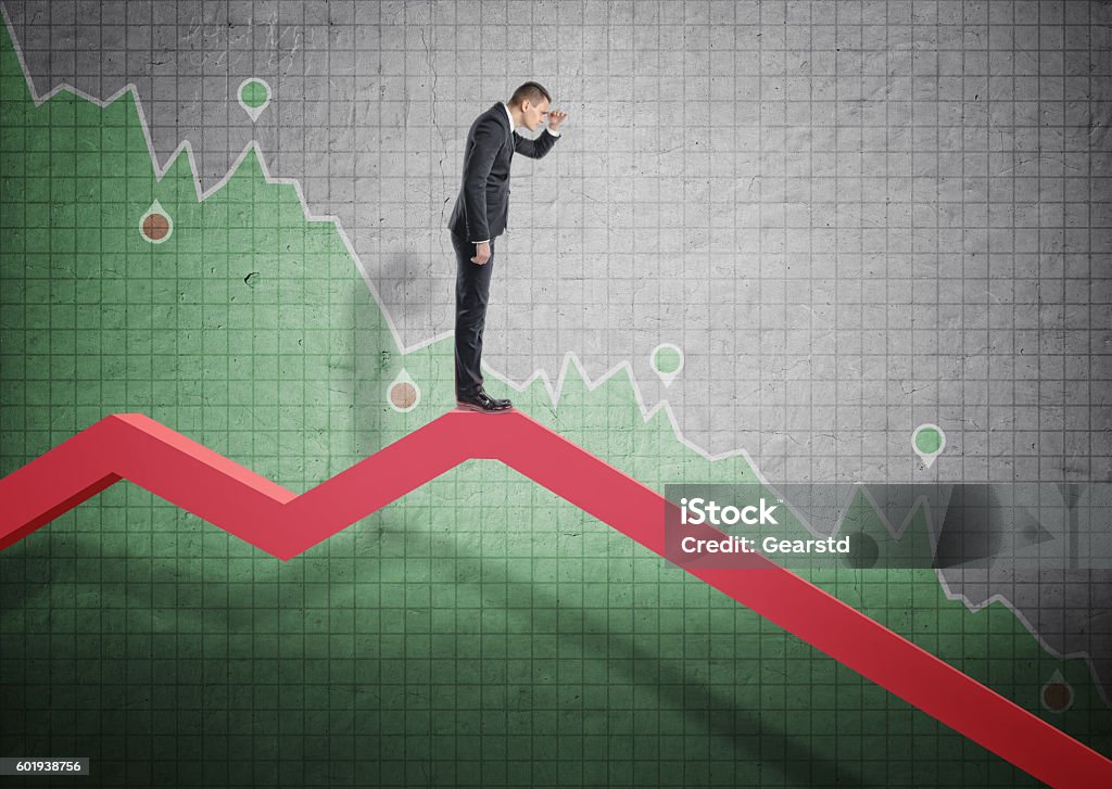 Businessman standing on falling diagram and peering into the future Businessman standing on falling diagram and peering into the future on the background of stock market selloff. Economic crisis. Bankruptcy and money devaluation. Stock Market and Exchange Stock Photo