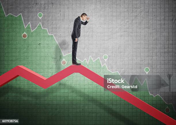 Businessman Standing On Falling Diagram And Peering Into The Future Stock Photo - Download Image Now