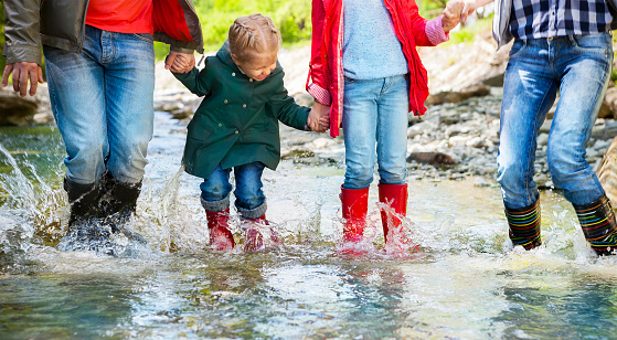 Happy family wearing rain boots jumping into a mountain river