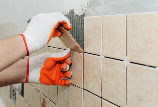 Worker sets  tiles on the wall in the kitchen. His hands are placing the tile on the adhesive.