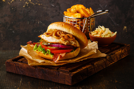 Burger with chicken breast and fried onions with coleslaw and potato wedges on dark background