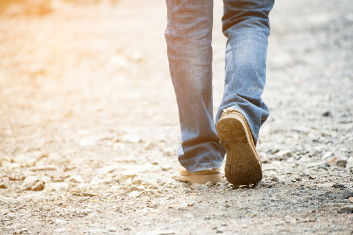 Lonely man wearing jeans and leather boots walking along the path strewn with rocks.