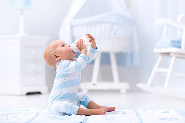 Baby boy drinking milk from a bottle in sunny nursery
