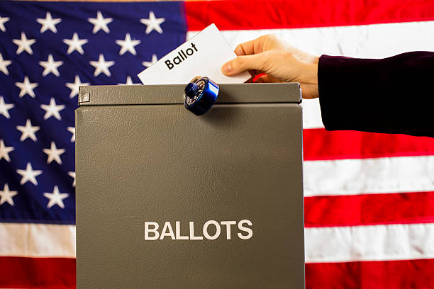 istock Voter inserting ballot into box with USA flag background. 602292080
