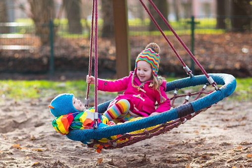 Little boy and girl on a playground. Child playing outdoors in autumn. Kids play on school yard. Happy kid in kindergarten or preschool. Children having fun on cold fall day. Toddler on a swing.