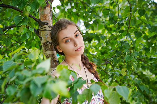 Portrait of a beautiful young woman on a background of green foliage in the summer park