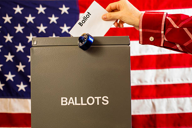 istock Voter inserting ballot into box with USA flag background. 602296566