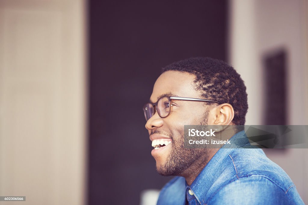 Afro american young man smiling, side view Afro american young man wearing denim shirt and glasses, smiling. Side view. Indoor shot. African-American Ethnicity Stock Photo