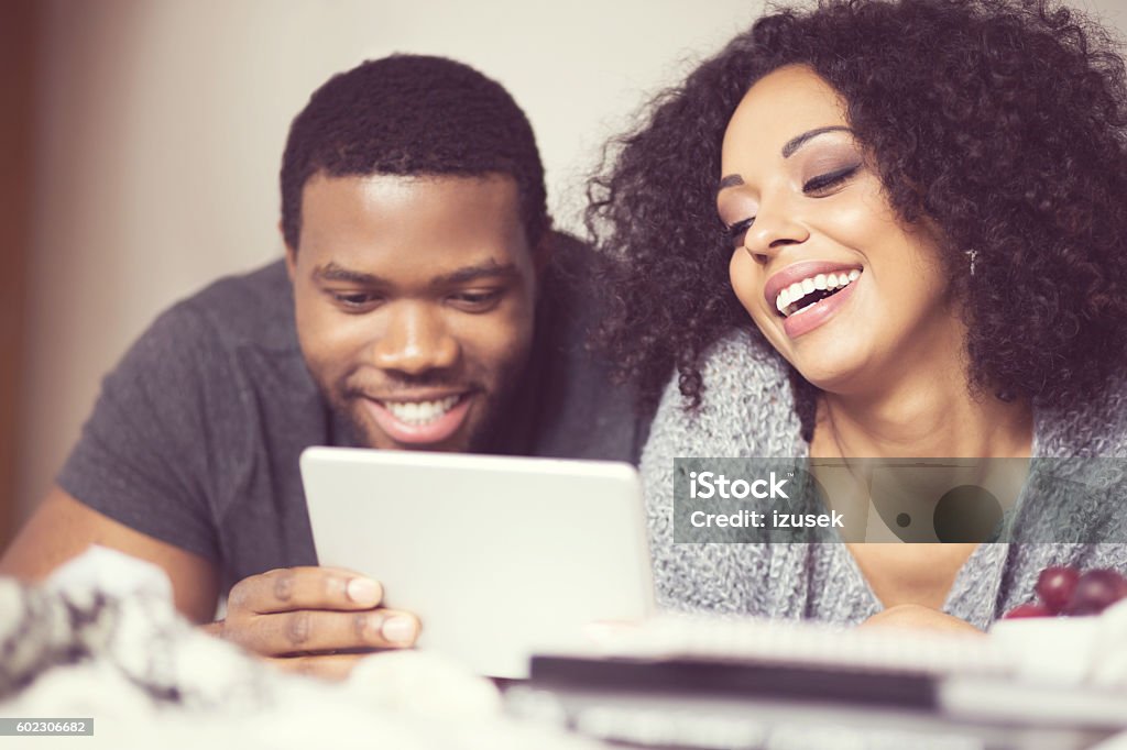 Afro american couple using a digital tablet Happy afro american friendly couple lying on bed at home and using a digital tablet. Close up of faces.  Adult Stock Photo