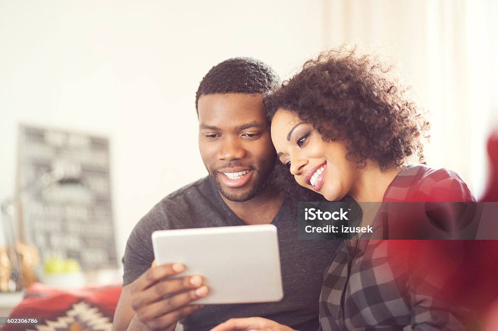 Afro american happy couple using a digital tablet at home Afro american friendly couple sitting on sofa at home and using a digital tablet. Adult Stock Photo