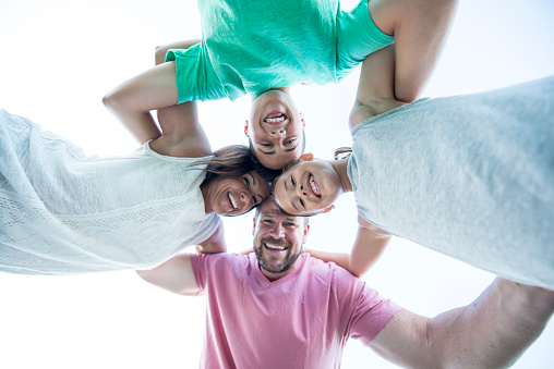 A family of four is standing together in a huddle and are smiling while looking down at the camera.