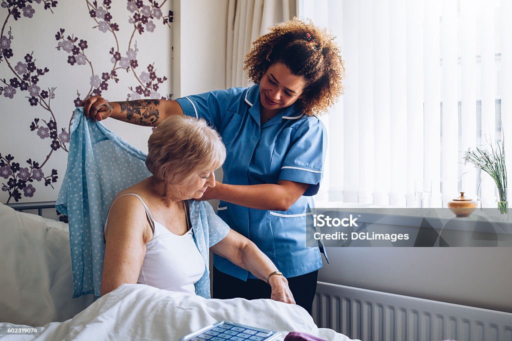 Home caregiver dressing senior Home Caregiver helping a senior woman get dressed in her bedroom. Home Caregiver Stock Photo