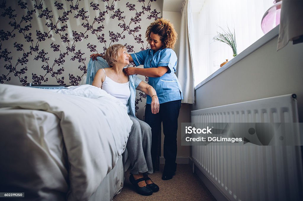 Home caregiver dressing senior Home Caregiver helping a senior woman get dressed in her bedroom. Nursing Home Stock Photo