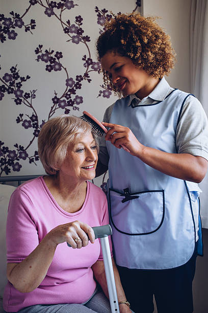 Carer Brushing Patients Hair Home Caregiver brushing the hair of a senior woman in her bedroom. nurse smock stock pictures, royalty-free photos & images