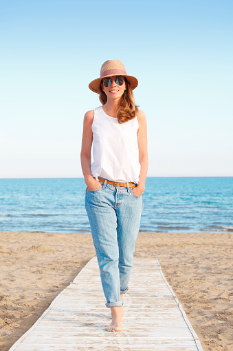 Full length portrait of smiling woman enjoying sun on vacation while walking on the beach.