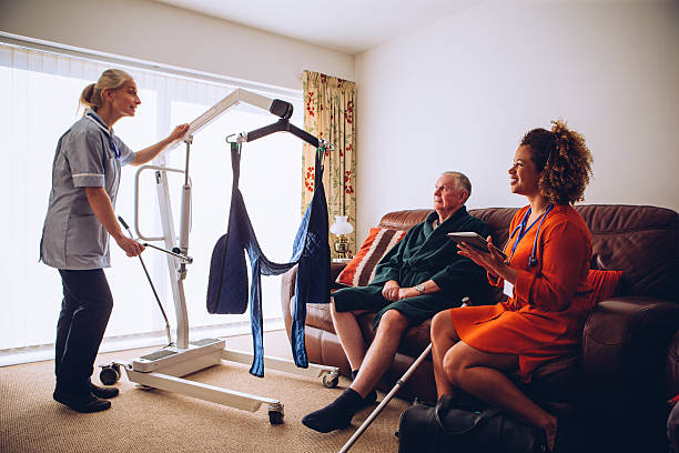 Homecare Workers preparing Hoist Two homecare nurses at an elderly mans house. They have a hoist set up. hoisting photos stock pictures, royalty-free photos & images