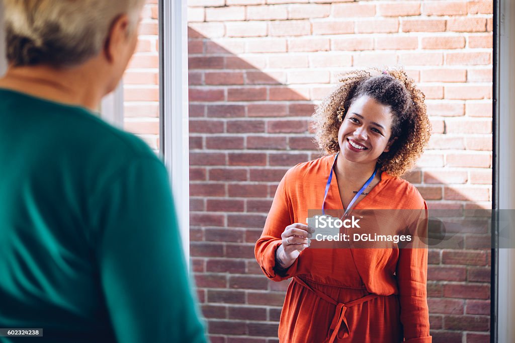 I'll be helping you today! Healthcare worker showing her badge at the front door of a senior womans home. Community Outreach Stock Photo